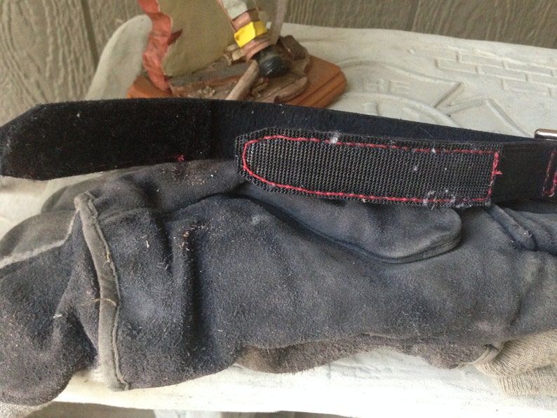 May include: Black adjustable strap with a red stitching detail. The strap is made of a durable material and has a secure closure.