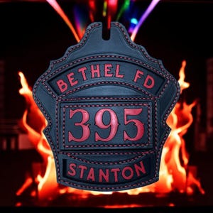 May include: A black leather firefighter helmet shield with red stitching and lettering. The shield reads "BETHEL FD" at the top, "395" in the center, and "STANTON" at the bottom. The background features flames.