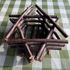 May include: A decorative container constructed from dark brown, natural wooden twigs arranged in a hexagonal, interlocking log cabin pattern. The structure features multiple layers of horizontal sticks stacked to form a hollow, open-top vessel.