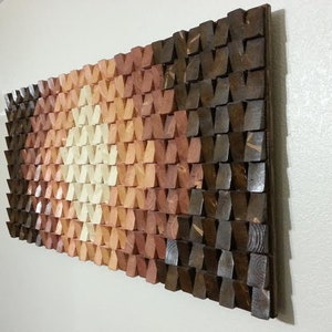 May include: A wall art piece made of wood with a geometric pattern. The wood is stained in shades of brown, orange, and white. The piece is mounted on a white wall.