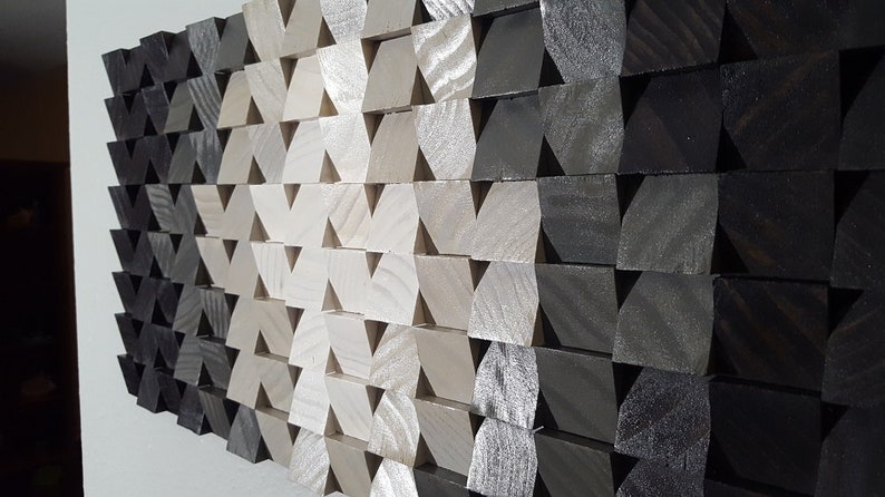 May include: A wall art piece made of wood with a geometric pattern of triangles. The triangles are arranged in a gradient pattern, starting with black and transitioning to white.