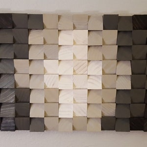 May include: A wall art piece made of wood blocks in various shades of gray and white. The blocks are arranged in a gradient pattern, with the darkest shades of gray on the edges and the lightest shades of white in the center. The blocks are all the same size and shape, and they are arranged in a staggered pattern.