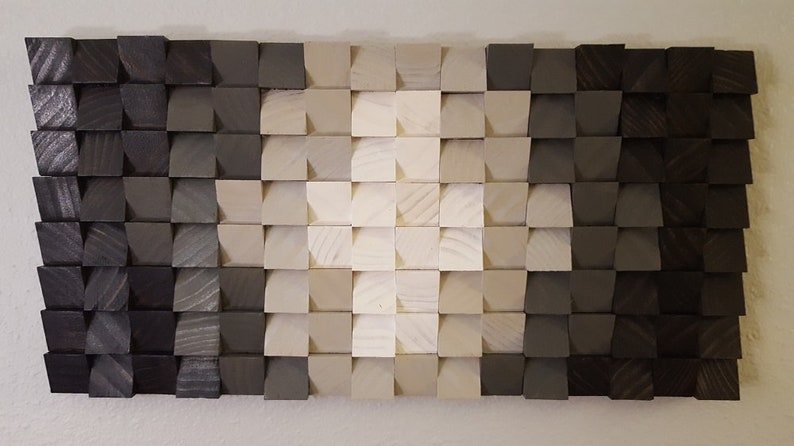 May include: A wall art piece made of wood blocks in various shades of gray and white. The blocks are arranged in a gradient pattern, with the darkest shades of gray on the edges and the lightest shades of white in the center. The blocks are all the same size and shape, and they are arranged in a staggered pattern.