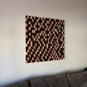 May include: A wall-mounted geometric art piece made of wood. The piece is composed of a grid of squares, each of which is made up of two triangles. The triangles are alternating colors of black and brown.