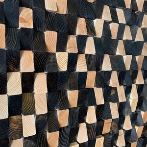 May include: A wall art piece made of wood blocks in a staggered pattern. The blocks are painted in black and natural wood tones, creating a geometric design.