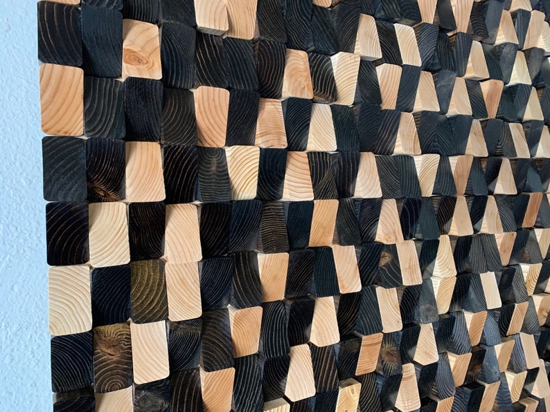 May include: A wall art piece made of wood blocks in a staggered pattern. The blocks are painted in black and natural wood tones, creating a geometric design.