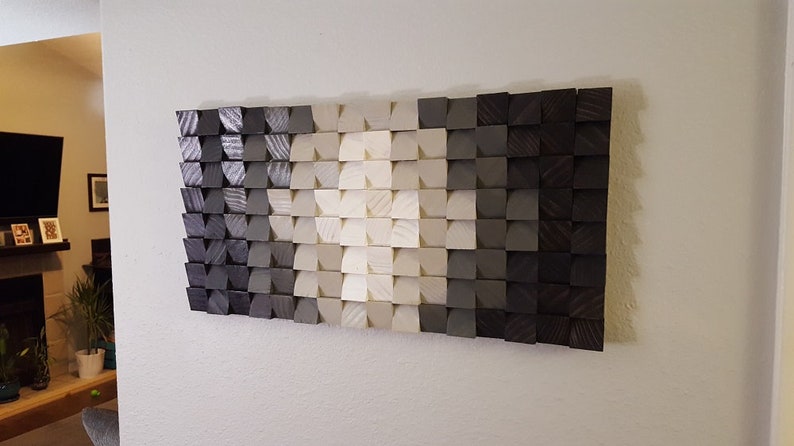 May include: A wall art piece made of wood blocks in various shades of gray, white, and black. The blocks are arranged in a geometric pattern, creating a gradient effect.