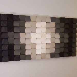 May include: A wall art piece made of wood blocks in shades of gray and white. The blocks are arranged in a gradient pattern, creating a modern and abstract design.