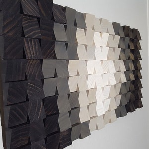May include: A wall art piece made of wood blocks in shades of black, gray, and white. The blocks are arranged in a geometric pattern, creating a modern and abstract design.