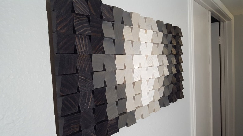 May include: A wall art piece made of wood blocks in shades of black, gray, and white. The blocks are arranged in a geometric pattern, creating a modern and abstract design.