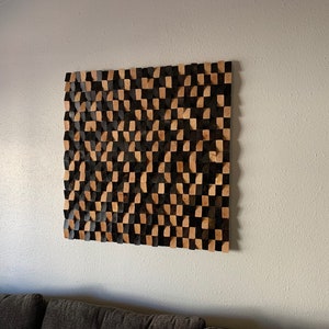May include: A wall-mounted acoustic panel made of wood blocks in a checkerboard pattern of black and natural wood.