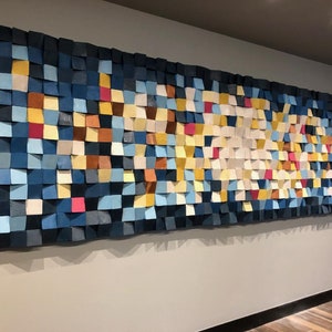 May include: A large wall art piece made of wood squares in various shades of blue, yellow, white, brown, and pink. The squares are arranged in a pattern that creates a sense of movement and depth.