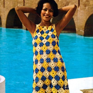 May include: A woman wearing a crocheted dress with a geometric pattern in shades of blue, yellow, and white. The dress has a sleeveless design and a scalloped hemline.