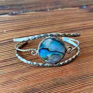 May include: Silver cuff bracelet with a round abalone shell inlay. The bracelet has a hammered texture and a twisted wire design.