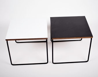 May include: Two square end tables with black metal frames. One table has a white top and the other has a black top.