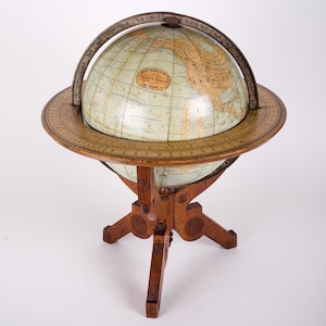 May include: A vintage wooden globe with a light green map and a brass meridian ring. The globe is on a wooden stand with a decorative base.
