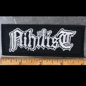 May include: White embroidered patch on a black background with the word "Ahilia" in a gothic font.