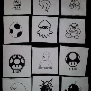 May include: A set of 12 iron-on patches featuring various cartoon characters and designs, including a mushroom with "1 UP" text, a ghost, a bomb, a squid, a turtle, a character from the Peanuts comic strip, and a character from the animated series "King of the Hill".