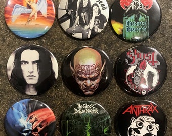 May include: Nine round metal pinback buttons with various band logos. The buttons feature images of musicians, band names, and album art. The bands include Motorhead, Dark Angel, Ghost, The Black Dahlia Murder, and Anthrax.