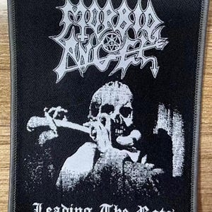 May include: Black and white embroidered patch with the band name "Morbid Angel" in a gothic font. The patch features a skull with a sword in its hand and the text "Leading The Rats" at the bottom.