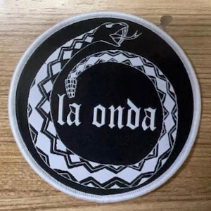 May include: Black and white embroidered patch with a snake design and the text "la onda" in a stylized font.