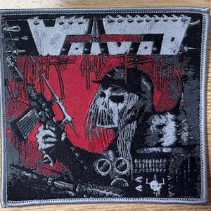 May include: A black and gray embroidered patch with the band name "VOW" and the words "Fight And Run" in a stylized font. The patch features a figure holding a rifle with a red background.