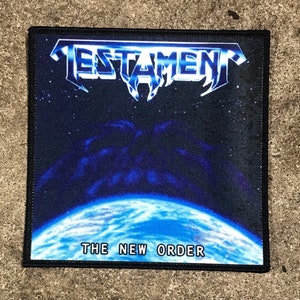 May include: A black and blue embroidered patch with the band name "TESTAMENT" and the album title "THE NEW ORDER" in white text. The patch features a blue planet with a dark blue nebula in the background.