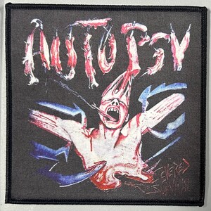 May include: A black and white patch with a graphic of a person with their head ripped open and intestines spilling out. The word "AUTOPSY" is written in red and white letters above the graphic.