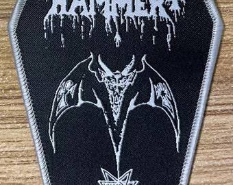May include: A black and white embroidered patch with the text "HEGIAL HAMMER" and "Satanic Rites" in a gothic font. The patch features a pentagram and a winged demon.