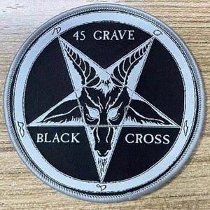 May include: Round black patch with a silver border. The patch features a white pentagram with a goat's head in the center. The words "45 GRAVE" and "BLACK CROSS" are written in white around the pentagram.