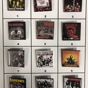 May include: A collection of twelve square pinback buttons featuring album art from punk rock bands The Exploited and Ramones. The buttons display album covers with text and band member images.
