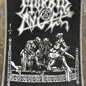 May include: Black patch with white embroidered text and imagery. The top text reads "MORBID ANGEL" in a stylized font. Below, a detailed illustration depicts figures on a bed. The bottom text reads "ABOMINATIONS OF DESOLATION".
