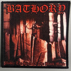 May include: Black and red embroidered patch with the band name "BATHORY" in a gothic font. The image features a figure with horns and a red background. The text "Under The Sign Of The Black Mark" is at the bottom of the patch.