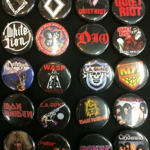 May include: A collection of 18 round black and white buttons with various rock band logos and names. The buttons feature bands such as Quiet Riot, Dio, WASP, Iron Maiden, and KISS.