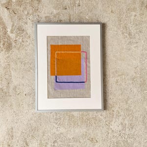 May include: Framed abstract art piece featuring layered geometric shapes in orange, purple, and blue. The artwork is set against a neutral linen background, encased in a white mat and a silver frame. The composition is modern and minimalist.
