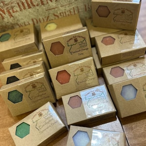 May include: A collection of boxed soaps with visible hexagonal soap shapes. The boxes are brown with a clear window showing the soap color. The labels read "Honey Pot Herbals" and list soap varieties like "Patchouli Orange" and "Eucalyptus Spearmint Soap."