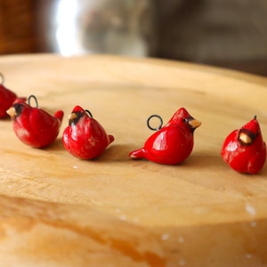May include: Five small ceramic cardinal bird ornaments in red with black eyes and beaks. The ornaments have a loop for hanging.