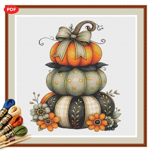 May include: A cross-stitch pattern featuring a stack of three pumpkins. The top pumpkin is orange with a light green bow, the middle is sage green with yellow polka dots, and the bottom is black and white with floral accents and orange flowers.