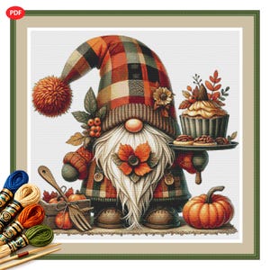 May include: A cross-stitch pattern featuring a gnome wearing a plaid hat with a pom-pom, holding a tray with a cupcake. The gnome has a long white beard, a flower accent, and stands next to a wooden crate with a fork and a pumpkin.