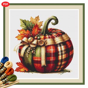 May include: A cross-stitch pattern featuring a pumpkin decorated with red, green, and orange plaid fabric segments, accented by autumn leaves, a burlap ribbon, and two wooden buttons. The design includes a set of colorful embroidery floss skeins.