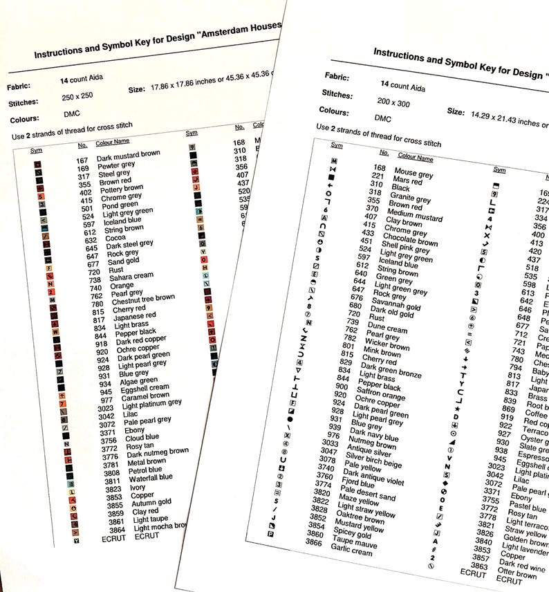 May include: Two white paper instruction sheets for cross stitch patterns titled Amsterdam Houses. Each sheet displays a table with symbols, DMC thread numbers, and color names like dark mustard brown, pewter grey, and black, with dimensions.