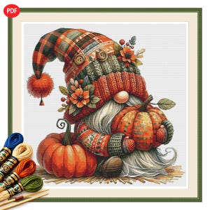 May include: A cross-stitch pattern featuring a gnome wearing a plaid and knit hat with a pom-pom, holding a pumpkin, and sitting next to another pumpkin. The design includes autumn flowers and is accompanied by several skeins of embroidery thread.