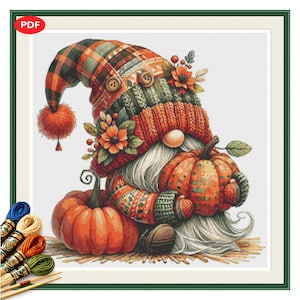 May include: A cross-stitch pattern featuring a gnome wearing a plaid hat with a pom-pom, two buttons, and floral accents. The gnome has a long white beard and holds a plaid pumpkin, with a second orange pumpkin beside it. Embroidery floss is shown.