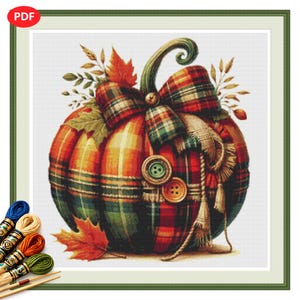 May include: A cross-stitch pattern featuring a pumpkin with a red, green, and yellow plaid design, adorned with a plaid bow, two round buttons, and autumn leaves. The design includes a frayed fabric accent and is accompanied by embroidery floss.