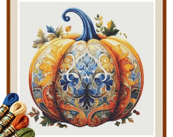 Op de afbeelding: Een kruissteekpatroon met een centrale pompoen met een blauwe steel, versierd met ingewikkelde blauwe, oranje en gele bloem- en krulmotieven, omringd door herfstbladeren, vergezeld van verschillende strengen borduurgaren.