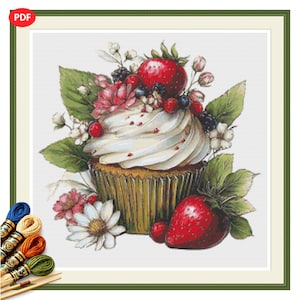 Puede incluir: Un patrón de punto de cruz que muestra un cupcake con glaseado blanco, fresas rojas, moras y flores blancas. El cupcake está en un molde verde plisado, rodeado de hojas verdes y bayas adicionales. Se ven madejas de hilo para bordar.