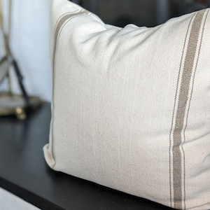 May include: A white throw pillow with two brown stripes down the center. The pillow is on a black surface.