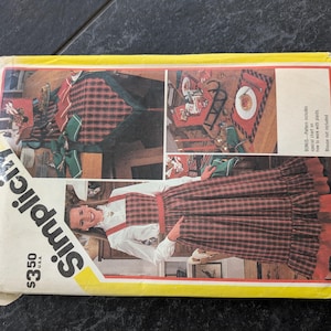 May include: A Simplicity sewing pattern for a plaid skirt and matching table runner and placemats. The pattern is for size 33 1/2 and includes instructions for making a skirt with a ruffle, a table runner, and placemats. The pattern is on a yellow background with a picture of a woman wearing the skirt and a table setting with the runner and placemats.