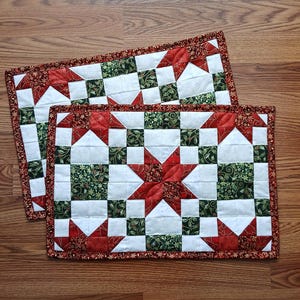 May include: Two red and green quilted placemats with a star pattern. The placemats have a red border with gold accents.