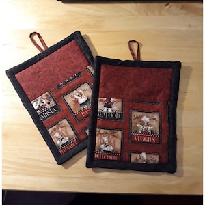 May include: Two square, quilted pot holders with a red background and black trim. Each pot holder has a loop for hanging and features images of chefs and food labels like "Pasta" and "Seafood".